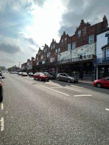 A street view shows a two-story brick building with shops on the ground level and windows above. Located at 38 & 38A Alexandra Road, Cleethorpes DN35 8LE, this mixed-use investment property for sale by auction with Palace Auctions has cars parked along the road, creating a bright yet overcast ambiance.
