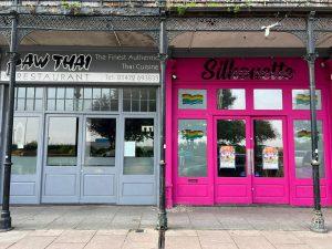 Storefronts of two adjacent businesses at 38 & 38A Alexandra Road, Cleethorpes DN35 8LE. On the left, "Saw Thai Restaurant" features a muted grey facade with windows. On the right, "Silhouette" has a bright pink exterior with rainbow flags in the windows. Mixed use investment property for sale by auction with Palace Auctions. Signs and posters