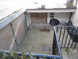 Property for sale by Auction A concrete courtyard at 3-4 Western Road & the Edinburgh mews TN37 6DG features a small puddle, scattered debris, and a covered motorcycle near a double-door garage. Flanked by stairs on the right and metal-grated doors on the left, some greenery adds a touch of nature in the bottom left corner. Presented by Palace Auctions