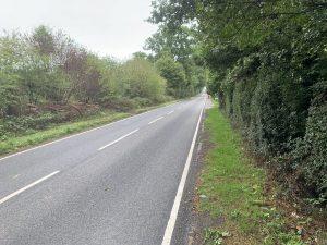 Property for sale by Auction A straight, empty road stretches into the distance, flanked by dense, green trees and bushes on both sides. Located near Plot 10 on Stane Street in Ockley, the smooth, freshly paved surface features crisp white lane markings. The surrounding area appears calm and lush with greenery. Presented by Palace Auctions