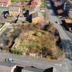 Property for sale by Auction An aerial view of Cradley Heath captures a residential neighborhood with pitched-roof houses, paved roads, and parked cars. The image centers on development land at Peartree—a fenced, overgrown lot with dense vegetation—contrasting sharply with the well-maintained properties surrounding it. Presented by Palace Auctions