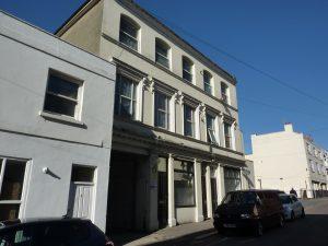 Property for sale by Auction A street view of a three-story beige building with white trim and large windows on the second and third floors at 3-4 Western Road, TN37 6DG. A small white building is adjacent on the left. Several cars, including a red van, are parked along the street. The sky is clear and blue. Presented by Palace Auctions