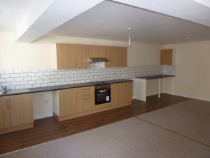 Property for sale by Auction Located at 3-4 Western Road, the spacious open-plan kitchen and living area features wooden flooring. The kitchen boasts light brown cabinets, a dark countertop, white subway tile backsplash, and built-in stainless steel appliances. The carpeted beige living area complements the overall aesthetic with its white walls. Presented by Palace Auctions