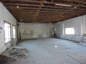 Property for sale by Auction A large, empty room at 3-4 Western Road & the Edingburugh mews TN37 6DG features an open wooden beam ceiling and white brick walls. The floor is dusty and scattered with torn carpet pieces and debris. Sunlight filters through two windows on the left wall and one window on the right wall. Presented by Palace Auctions