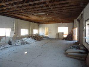 Property for sale by Auction A large, empty room with exposed wooden ceiling beams and debris on the floor at 3-4 Western Road & the Edinburgh mews TN37 6DG. Broken pieces of drywall, wood, and insulation are scattered along the walls. Sunlight enters through several windows, and a door is visible at the far end of the room. Presented by Palace Auctions