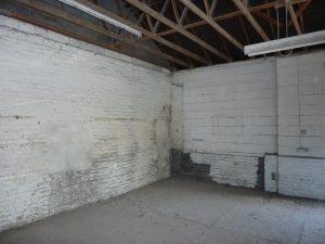 Property for sale by Auction An image of a vacant room at 3-4 Western Road & the Edinburgh mews TN37 6DG, with white-painted brick walls and a concrete floor. Exposed wooden beams run across the ceiling, and two fluorescent light fixtures hang from the beams. The room appears to be in a state of disrepair with some peeling paint and dirt on the floor. Presented by Palace Auctions