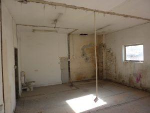 Property for sale by Auction An abandoned, dilapidated room with peeling walls and a dirty floor at 3-4 Western Road. A single toilet is visible in the rear left corner, and a broom leans against a pole in the center of the room. Light filters in through a small window on the right, partially illuminating the space. Presented by Palace Auctions