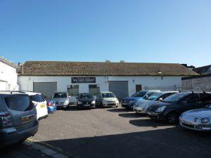 Property for sale by Auction A row of parked cars in front of a single-story building with a slanted roof. Above the building's entrance is a large banner that reads "WE HAVE MOVED to 3-4 Western Road, the Edingburugh mews TN37 6DG." The sky is clear and blue. Presented by Palace Auctions