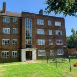 Property for sale by Auction A brick apartment building at 21 Glazebrook Close, Dulwich, London, with four stories and numerous windows is set against a clear blue sky. In front, there's a small playground area with a slide, grass lawn, and a few benches. Trees and a fence are also visible around the perimeter of the building. Presented by Palace Auctions