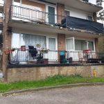 Property for sale by Auction A photo of a two-story, brick apartment building at 37 Farley Lodge, Bedfordshire, with balconies on both levels. The upper balcony has black tarpaulin covering its railing. The lower balcony in Luton is furnished with chairs, potted plants, and small decorations. The grass in front of the building is untidy. Presented by Palace Auctions