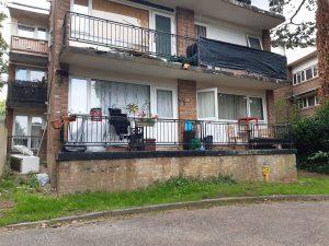Property for sale by Auction A photo of a two-story, brick apartment building at 37 Farley Lodge, Bedfordshire, with balconies on both levels. The upper balcony has black tarpaulin covering its railing. The lower balcony in Luton is furnished with chairs, potted plants, and small decorations. The grass in front of the building is untidy. Presented by Palace Auctions