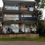 Property for sale by Auction A three-story residential building at 37 Farley Lodge in Luton, Bedfordshire, features balconies on each floor. The second-floor balcony has a large black covering, and the third-floor balcony has laundry hanging. Various items are visible on the balconies. The building is surrounded by trees and greenery. Presented by Palace Auctions