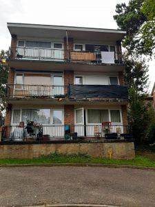 Property for sale by Auction A three-story residential building at 37 Farley Lodge in Luton, Bedfordshire, features balconies on each floor. The second-floor balcony has a large black covering, and the third-floor balcony has laundry hanging. Various items are visible on the balconies. The building is surrounded by trees and greenery. Presented by Palace Auctions