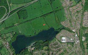 Property for sale by Auction Aerial view of a landscape featuring a large lake surrounded by greenery and fields. On the right, there is a residential area with clustered houses and a few larger buildings at Sevenoaks. A small red rectangle is visible near the center, not far from plots of land at 435 Chevening Road, TN13 2SA. Presented by Palace Auctions