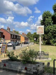 Property for sale by Auction A village scene with a sign that reads "Chipstead," indicating the village name. A row of traditional brick houses line the street under a partly cloudy blue sky. In the foreground, there's a wooden planter with flowers and a few benches nearby, near Sevenoaks' TN13 2SA area and plots of land at 435 Chevening Road. Presented by Palace Auctions