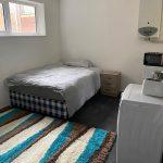 Property for sale by Auction A small bedroom at 37 Farley features a single bed against the wall, covered in grey bedding. Next to the bed is a wooden nightstand. At the foot of the bed is a washing machine with a small appliance on top. The floor is partially covered by a striped rug in brown, blue, and white. Presented by Palace Auctions
