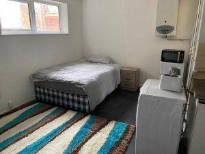 Property for sale by Auction A small bedroom at 37 Farley features a single bed against the wall, covered in grey bedding. Next to the bed is a wooden nightstand. At the foot of the bed is a washing machine with a small appliance on top. The floor is partially covered by a striped rug in brown, blue, and white. Presented by Palace Auctions