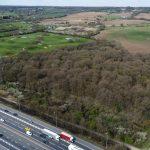 Property for sale by Auction Aerial views taken by drone reveal a highway with vehicles next to a dense wooded area bordered by expansive fields, including land at Epping Farm. The landscape features patches of green farmland and clusters of trees extending towards distant hills under a clear sky with scattered clouds. Presented by Palace Auctions
