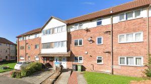 Property for sale by Auction A three-story brick investment apartment with white accents under a clear blue sky. Sold by its previous owner, it features three green trash bins along the walkway, a small white car parked near bushes, and windows with curtains. Other similar buildings are visible on the left. Presented by Palace Auctions
