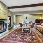 Property for sale by Auction A cozy living room on Bentley Road in Holmfirth featuring a stone fireplace with a lit fire, large wooden beams, and two plush red sofas with cushions. A wooden coffee table sits on a patterned rug in the center. The walls are neutral, and natural light softly illuminates the space at HD9 4AP. Presented by Palace Auctions