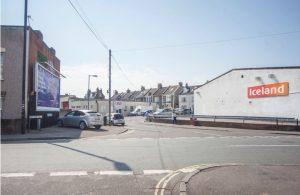 Property for sale by Auction A street corner with parked cars and shops on the land on north east side of Brixton Road, Bristol, BS5 0EL. A large white building on the right has an "Iceland" sign. Terraced houses are visible in the background. A billboard on the left side features an advertisement, and the sky is clear and bright. Presented by Palace Auctions
