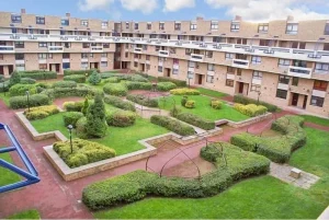 Property for sale by Auction A landscaped courtyard with neatly trimmed hedges, pathways, and cone-shaped topiary adorns the grounds of 159 Collingwood Court Washington. The area is surrounded by a multi-story brick apartment building, while outdoor benches and steel arch structures are spread throughout the greenery under a partly cloudy sky. Presented by Palace Auctions