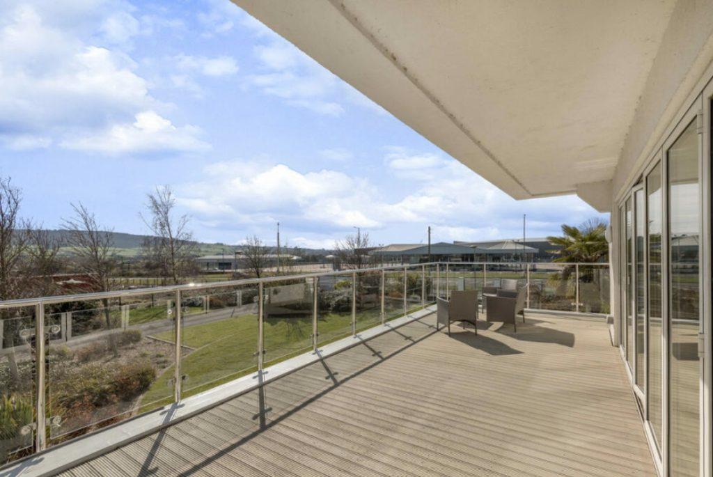 Property for sale by Auction A spacious balcony with glass railings and outdoor seating at Tindale Towers on Dilks Street overlooks a lush green landscape with trees and distant hills under a partly cloudy sky. The balcony, located in the Bishop DL14 9AP area, is connected to a building with large glass doors. Presented by Palace Auctions