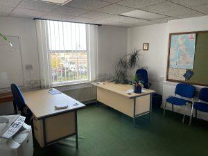 Property for sale by Auction A small office with two desks and blue chairs. One desk is near a window with blinds, the other against the wall with plants on it. Another plant is in the corner. There's a map and a clock on the wall, and a printer is visible in the foreground—an ideal setup for discussing available investment properties for sale by auction. Presented by Palace Auctions