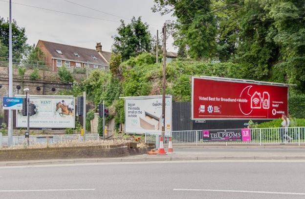 Property for sale by Auction A roadside scene features three billboards. The left billboard advertises Kent as the garden of England. The center billboard promotes a TV series. The right billboard highlights a plot of land with hope value for planning consent sold, boasting the slogan "Voted Best for Broadband and Mobile. Presented by Palace Auctions