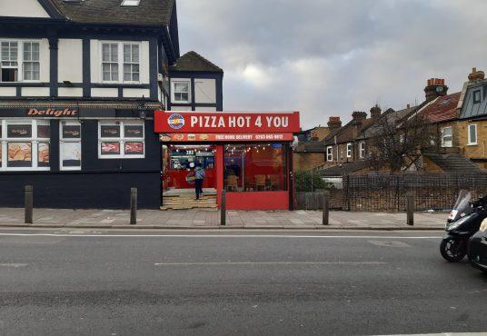 Property for sale by Auction A street view of "Pizza Hot 4 You," a pizza shop with a red and white storefront in a mixed commercial and residential area. The building, featuring black trim, is next to homes, making it an attractive leasehold investment property. A man on a motorcycle rides past the shop on the road. Presented by Palace Auctions