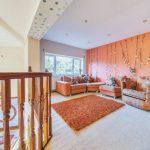 Property for sale by Auction A cozy living room on Rowan Avenue with an orange-themed décor. The space features an orange sectional sofa, a matching armchair, and a rectangular orange rug. The walls are partly orange with hanging bead decorations. Natural light streams in through large windows overlooking greenery. Presented by Palace Auctions