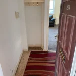 Property for sale by Auction A front door at 159 Collingwood Court, Washington is open, revealing a small entryway with hooks on the wall and a red-striped rug on the floor. Beyond the entryway, a view of a living room with a black sofa near a window is visible. Presented by Palace Auctions