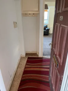 Property for sale by Auction A front door at 159 Collingwood Court, Washington is open, revealing a small entryway with hooks on the wall and a red-striped rug on the floor. Beyond the entryway, a view of a living room with a black sofa near a window is visible. Presented by Palace Auctions