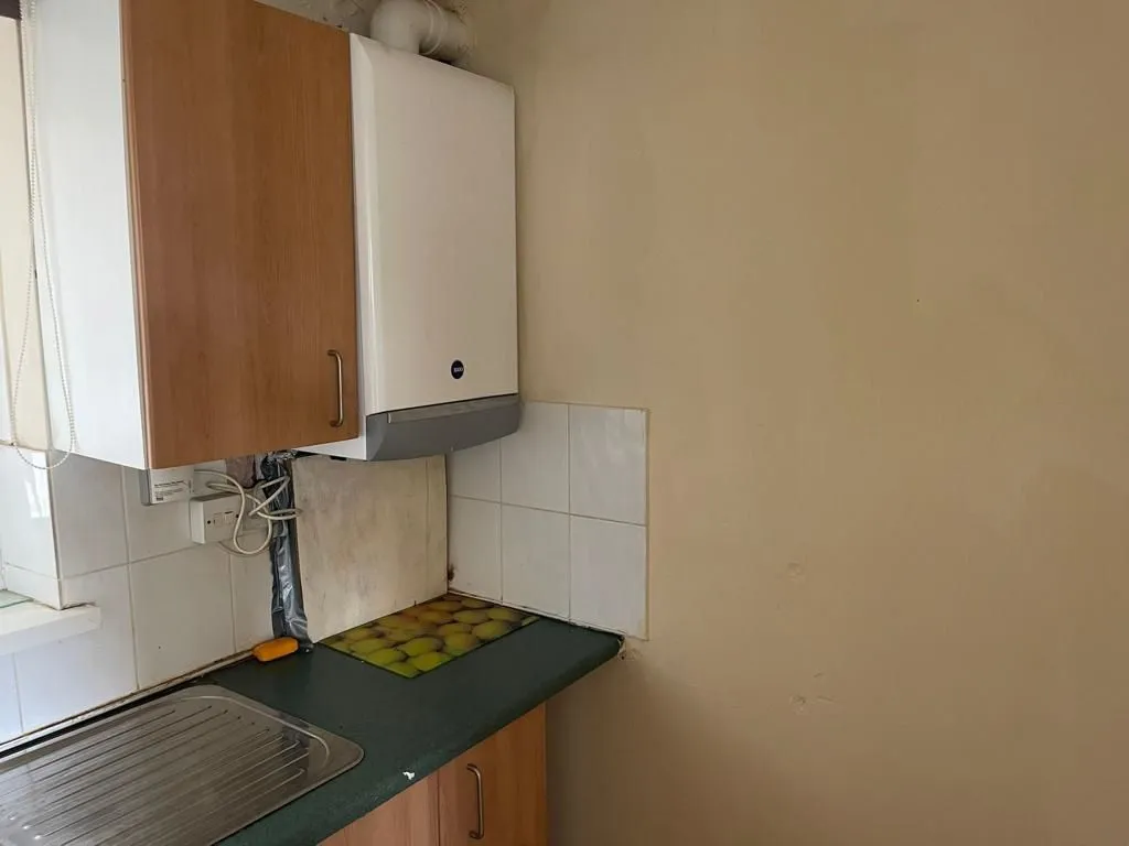Property for sale by Auction A small kitchen at 159 Collingwood Court, Washington, with a beige wall and wooden cabinets. A white boiler is mounted above the green counter, which holds several apples arranged in a row and is partially tiled with white ceramic tiles. Part of a stainless steel sink is visible. Presented by Palace Auctions