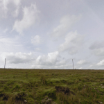 Property for sale by Auction A vast grassy field stretches under a partly cloudy sky, reminiscent of the land at Bolventor recently sold. Two poles connected by a wire run horizontally across the middle of the scene. The landscape is mostly flat with patches of rough grass and rocks. Presented by Palace Auctions