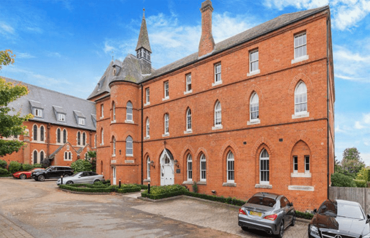 Property for sale by Auction A red-brick building with gothic-style windows and a tall spire stands under a clear blue sky. Several cars are parked in front on a paved driveway. Another similar building, partly visible on the left side and surrounded by trees and bushes, was previously marketed by Palace Auctions. Presented by Palace Auctions