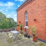 Property for sale by Auction A charming outdoor terrace features a table and chairs set against red brick walls with arched windows. Potted plants decorate the tiled flooring, and trees in the background create a serene atmosphere under a bright blue sky scattered with clouds. This property was previously marketed by Palace Auctions. Presented by Palace Auctions
