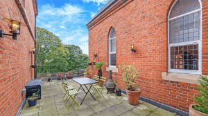 Property for sale by Auction A charming outdoor terrace features a table and chairs set against red brick walls with arched windows. Potted plants decorate the tiled flooring, and trees in the background create a serene atmosphere under a bright blue sky scattered with clouds. This property was previously marketed by Palace Auctions. Presented by Palace Auctions