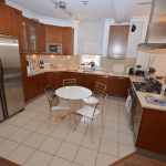 Property for sale by Auction A modern kitchen featuring wooden cabinets, stainless steel appliances, and a tiled floor. A round table with four metal chairs sits at the center. The kitchen also has a stove, microwave, refrigerator, and various kitchen items placed on the counters. Property previously marketed by Palace Auctions. Presented by Palace Auctions