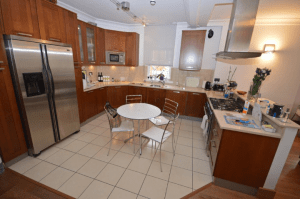 Property for sale by Auction A modern kitchen featuring wooden cabinets, stainless steel appliances, and a tiled floor. A round table with four metal chairs sits at the center. The kitchen also has a stove, microwave, refrigerator, and various kitchen items placed on the counters. Property previously marketed by Palace Auctions. Presented by Palace Auctions