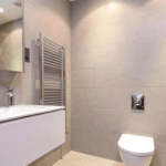 Property for sale by Auction A modern bathroom, previously marketed by Palace Auctions, features a wall-mounted toilet and a floating vanity with a sink and faucet. Above the vanity is a large mirrored cabinet. A heated towel rail is mounted on the wall to the left of the toilet, and neutral-colored tiles cover the walls and floor. Presented by Palace Auctions