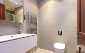 Property for sale by Auction A modern bathroom, previously marketed by Palace Auctions, features a wall-mounted toilet and a floating vanity with a sink and faucet. Above the vanity is a large mirrored cabinet. A heated towel rail is mounted on the wall to the left of the toilet, and neutral-colored tiles cover the walls and floor. Presented by Palace Auctions