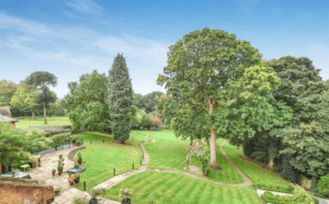 Property for sale by Auction A well-maintained garden, previously marketed by Palace Auctions, features a winding stone path, large trees, and neatly trimmed grass. Small shrubs and potted plants are scattered throughout the area. In the background, there's a brick wall and more greenery under a clear blue sky. Presented by Palace Auctions