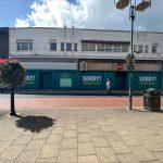Property for sale by Auction A commercial building in Crewe, Cheshire, with turquoise boards stating "SORRY! WE HAVE CLOSED," spans the width of the former Poundland sold by Palace Auctions. The surrounding area features a hanging flower basket, lamp posts, and a few pedestrians walking nearby. The sky above is partly cloudy. Presented by Palace Auctions
