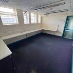 Property for sale by Auction An empty room with a purple carpet, white walls, and several windows letting in natural light. Located in a commercial building in Crewe Cheshire, this former Poundland — sold by Palace Auctions — features wall-mounted desks along the left and back walls and a coat rack near the door. Recessed lighting adorns the ceiling, but it appears to be in need of cleaning. Presented by Palace Auctions
