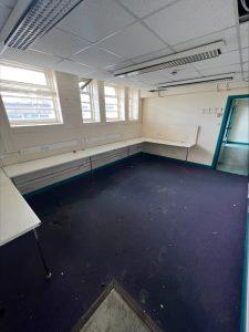 Property for sale by Auction An empty room with a purple carpet, white walls, and several windows letting in natural light. Located in a commercial building in Crewe Cheshire, this former Poundland — sold by Palace Auctions — features wall-mounted desks along the left and back walls and a coat rack near the door. Recessed lighting adorns the ceiling, but it appears to be in need of cleaning. Presented by Palace Auctions