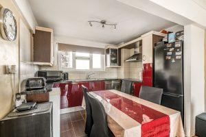 Modern kitchen in Flat 3 of Macclesfield House, Central Street LONDON EC1V 8BA, featuring a black refrigerator, black and white cabinets, stainless steel appliances, and a tiled backsplash. A black dining table with a red and beige tablecloth is surrounded by four black chairs. A wall clock is mounted to the left. Presented by Palace Auctions