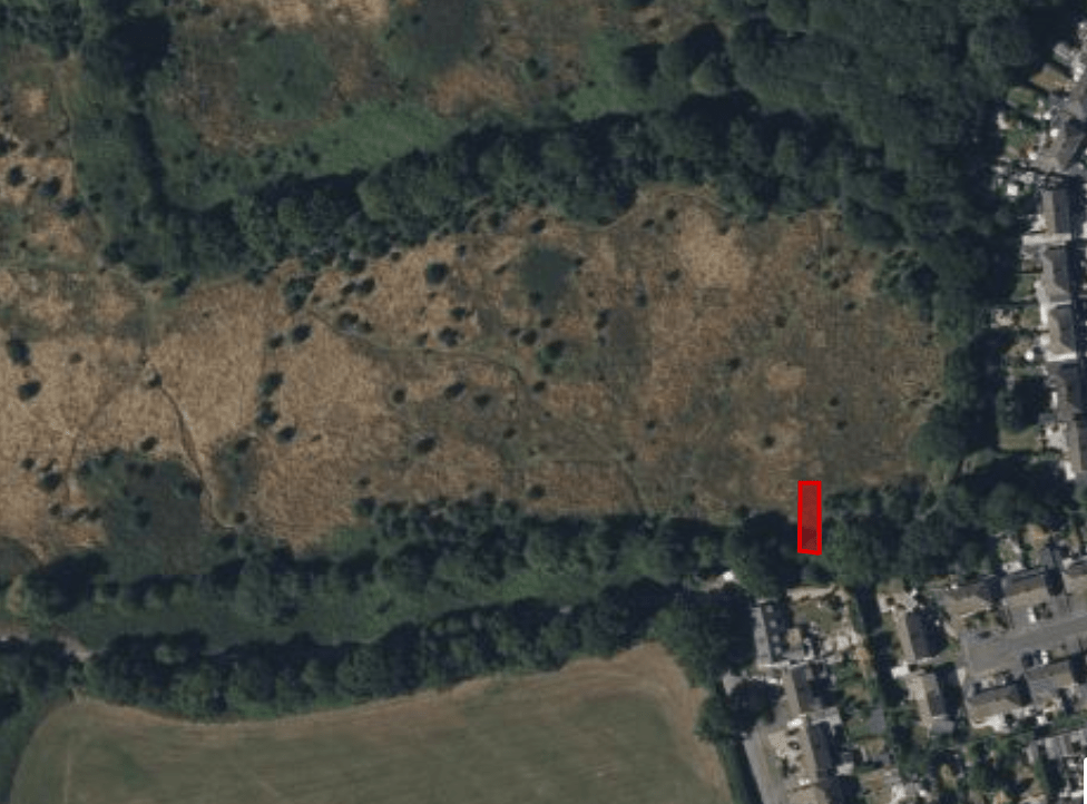Property for sale by Auction Aerial view of a landscape with a mix of open grassy areas and dense tree cover. The bottom-right shows a residential neighborhood with houses and streets. A red rectangle highlights a specific spot within the tree-lined section. Presented by Palace Auctions