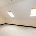 A small attic room with sloped ceilings features two skylight windows allowing natural light to flood in. The room, located in the charming Pools Cottages, Kenilworth, has beige walls, a light-colored carpet, and recessed lighting on the ceiling. This delightful space was CV8 2JW sold by auction with Palace Auctions.