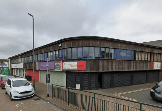 A two-story commercial building with wooden cladding and large windows on the upper floor is located on Trafalgar Street, Consett. Several business signs are displayed, and the lower storefronts have their shutters down. Cars are parked along the street under an overcast sky. The commercial investment property was sold by Palace Auctions.